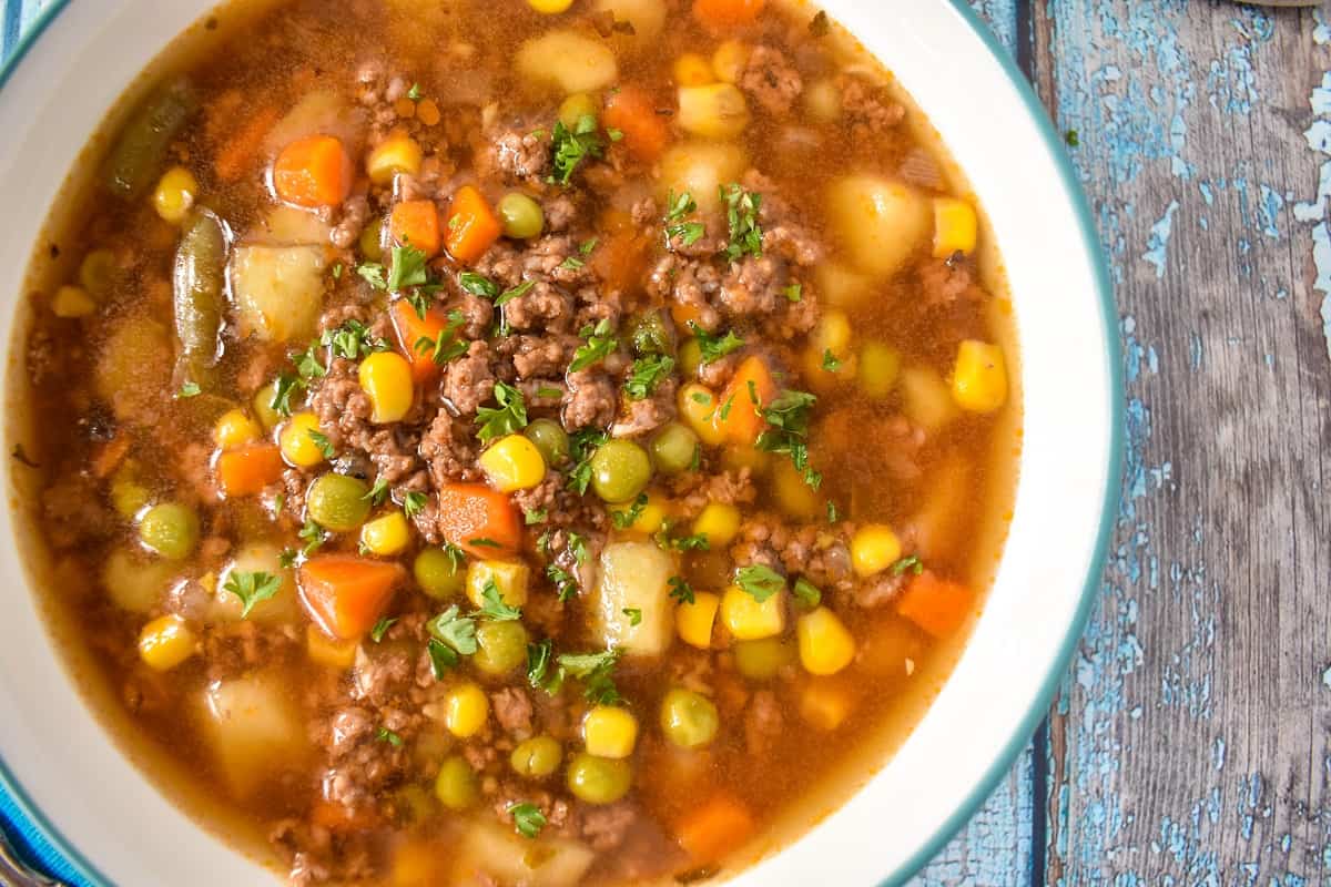 A close up of the hamburger soup served in a white bowl with a light blue rim.