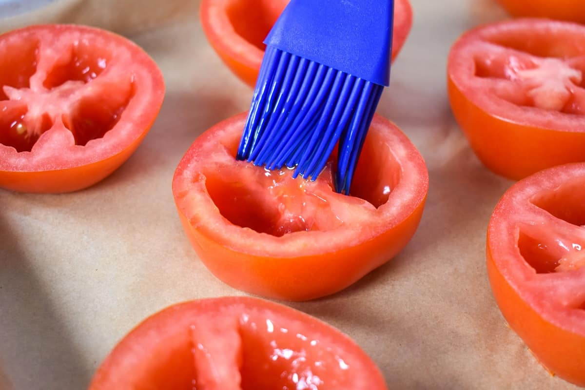 A blue silicone brush applying oil to a tomato half.