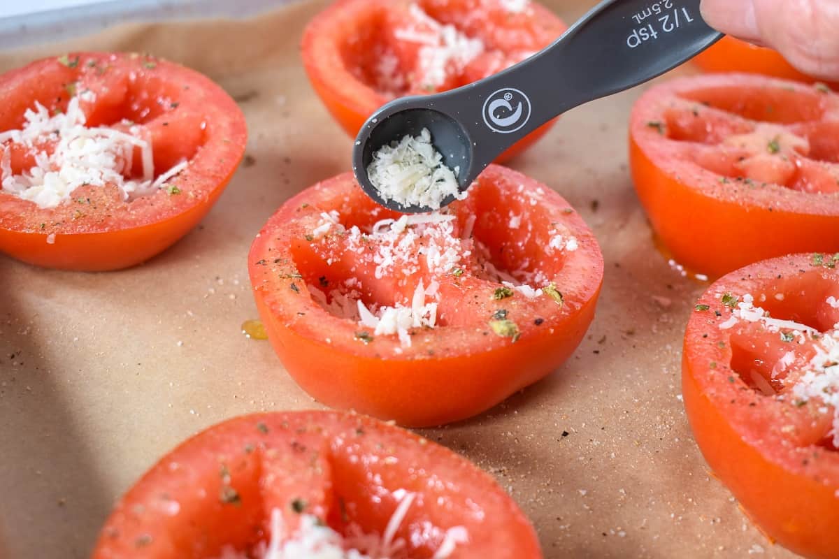 Grated parmesan being added to a hollowed out tomato half.