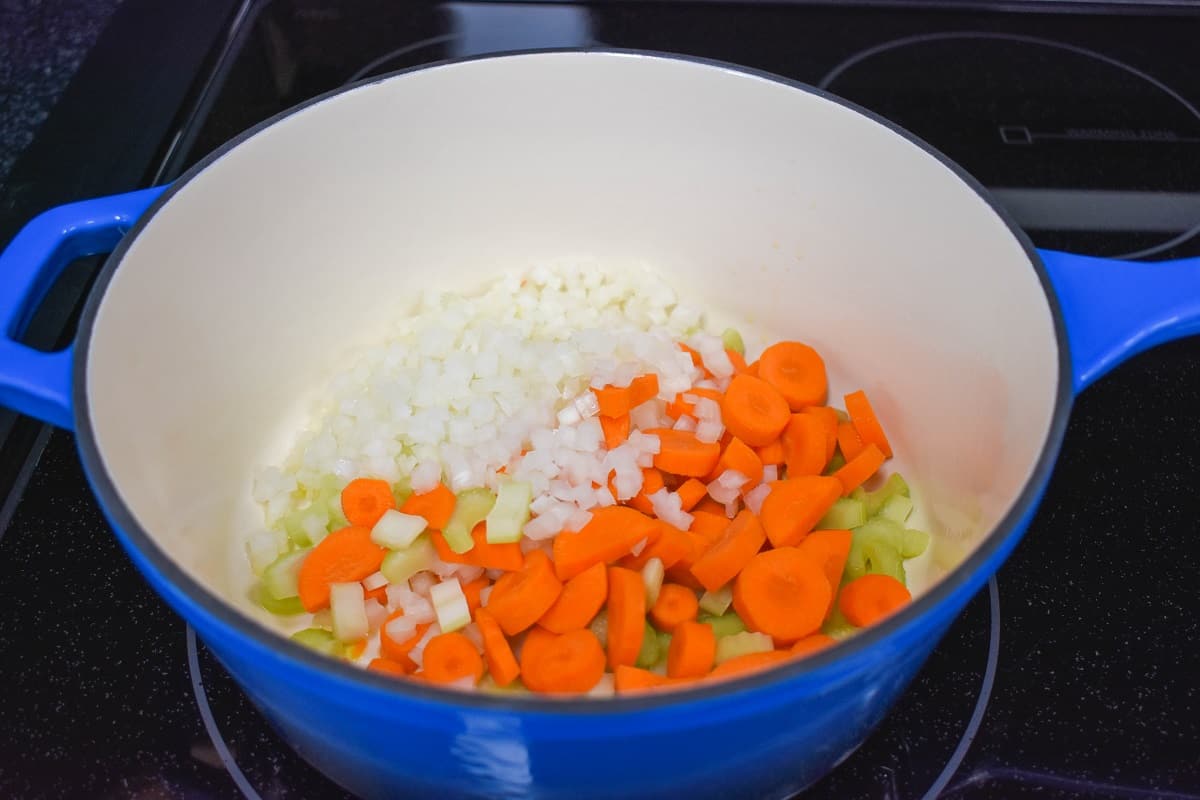 Onions, carrots, and celery cooking in a blue and white pot.