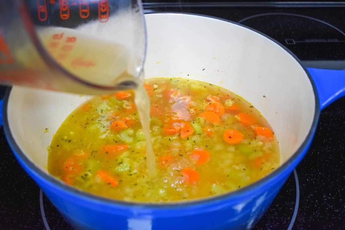 Chicken broth being added to the ingredients in the pot.