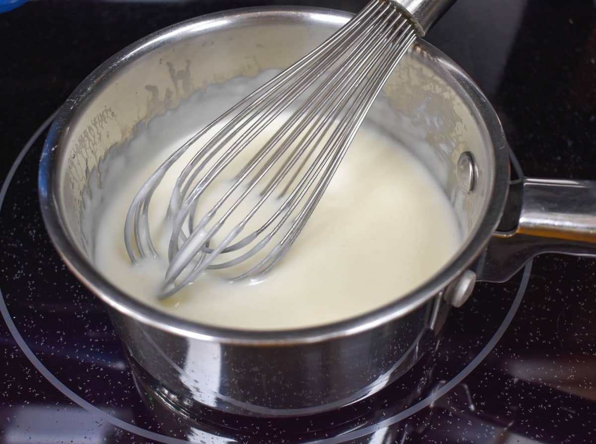 The white sauce in a saucepan with a whisk.