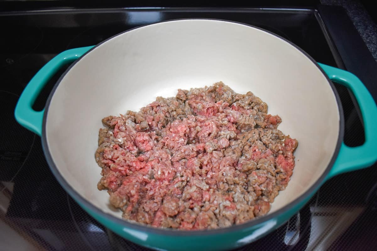 Ground beef cooking in a white and aqua pot.
