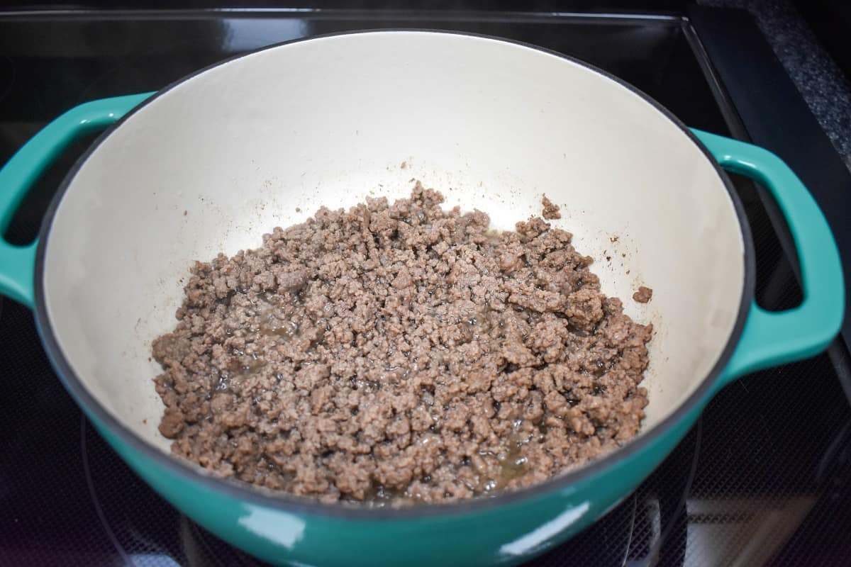 Browned ground beef cooking in a white and aqua pot.