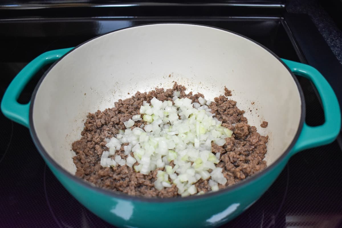 The browned ground beef with diced onion cooking in a white and aqua pot.
