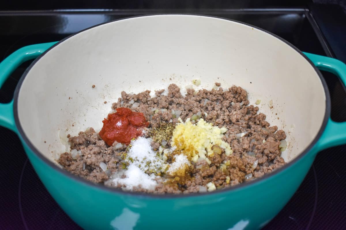 Ground beef with garlic, tomato paste, and spices in a white and aqua pot.
