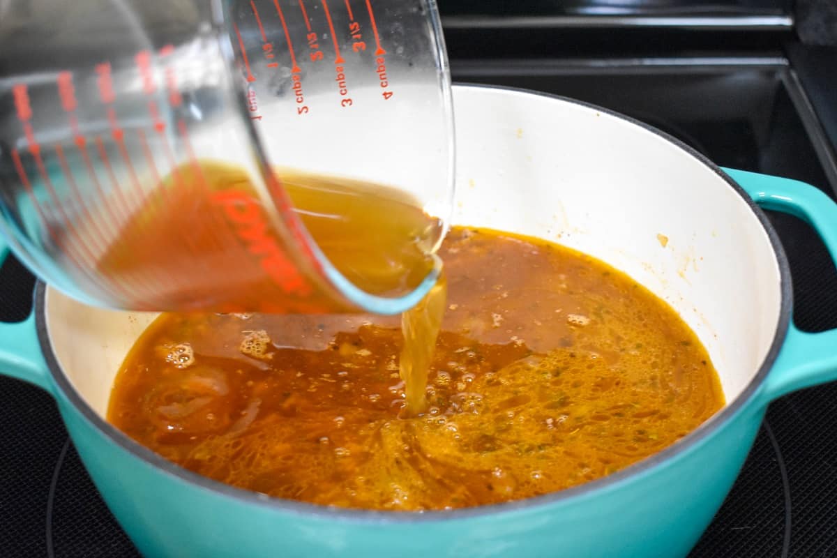 Beef broth being added to the ingredients in a large white and aqua pot.
