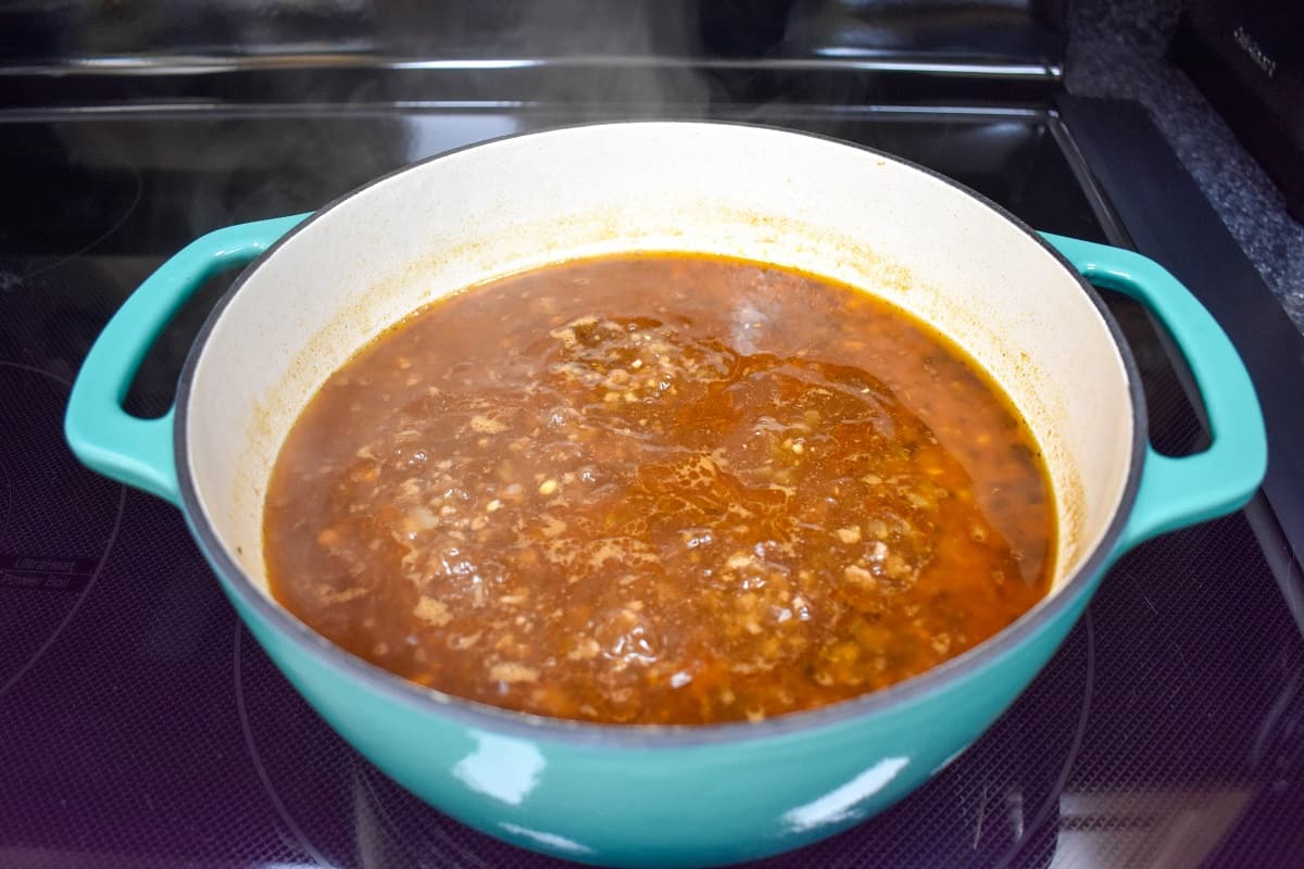 The soup simmering in a large white and aqua pot.