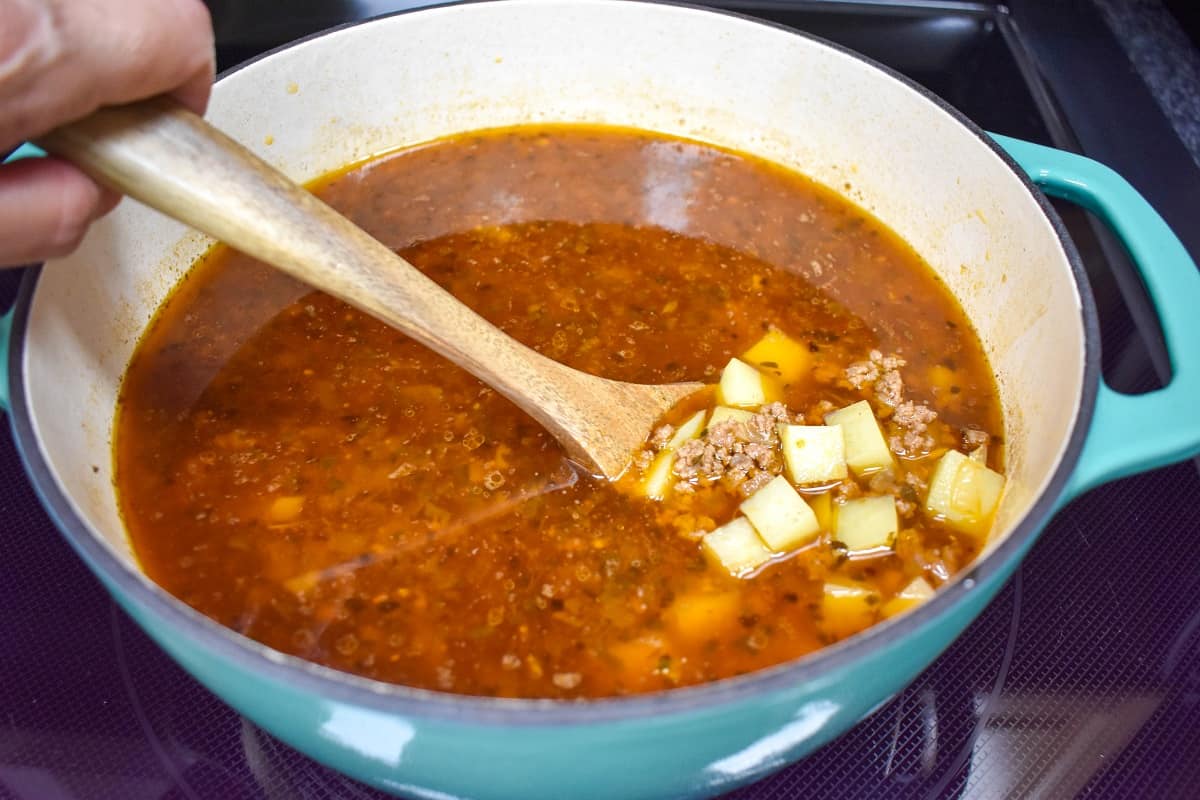 The pot of soup with diced potatoes held up with a wooden spoon.