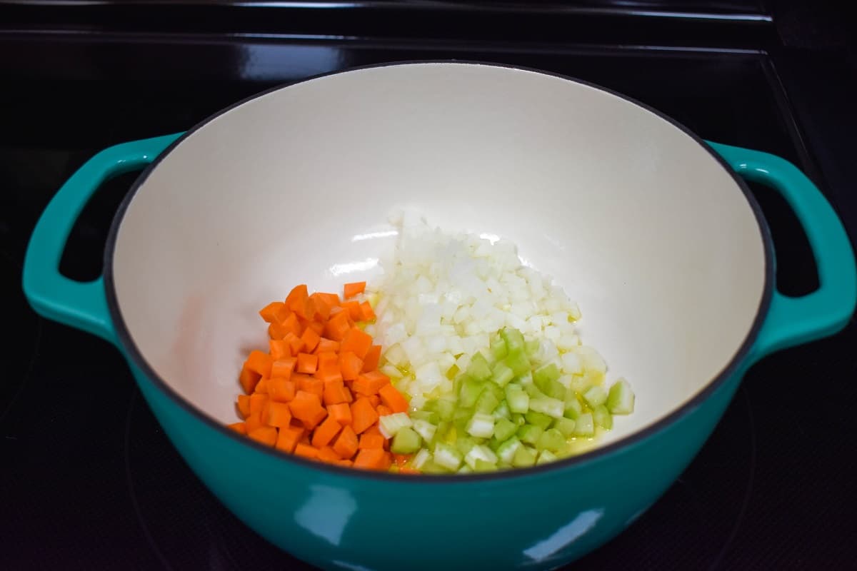 Onions, carrots, and celery in a white and light blue pot.