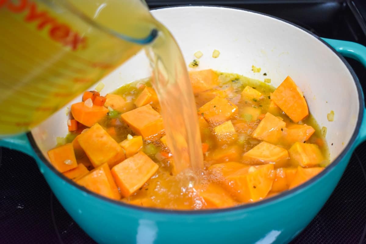 Chicken broth being added to cut sweet potato in a white and light blue pot.