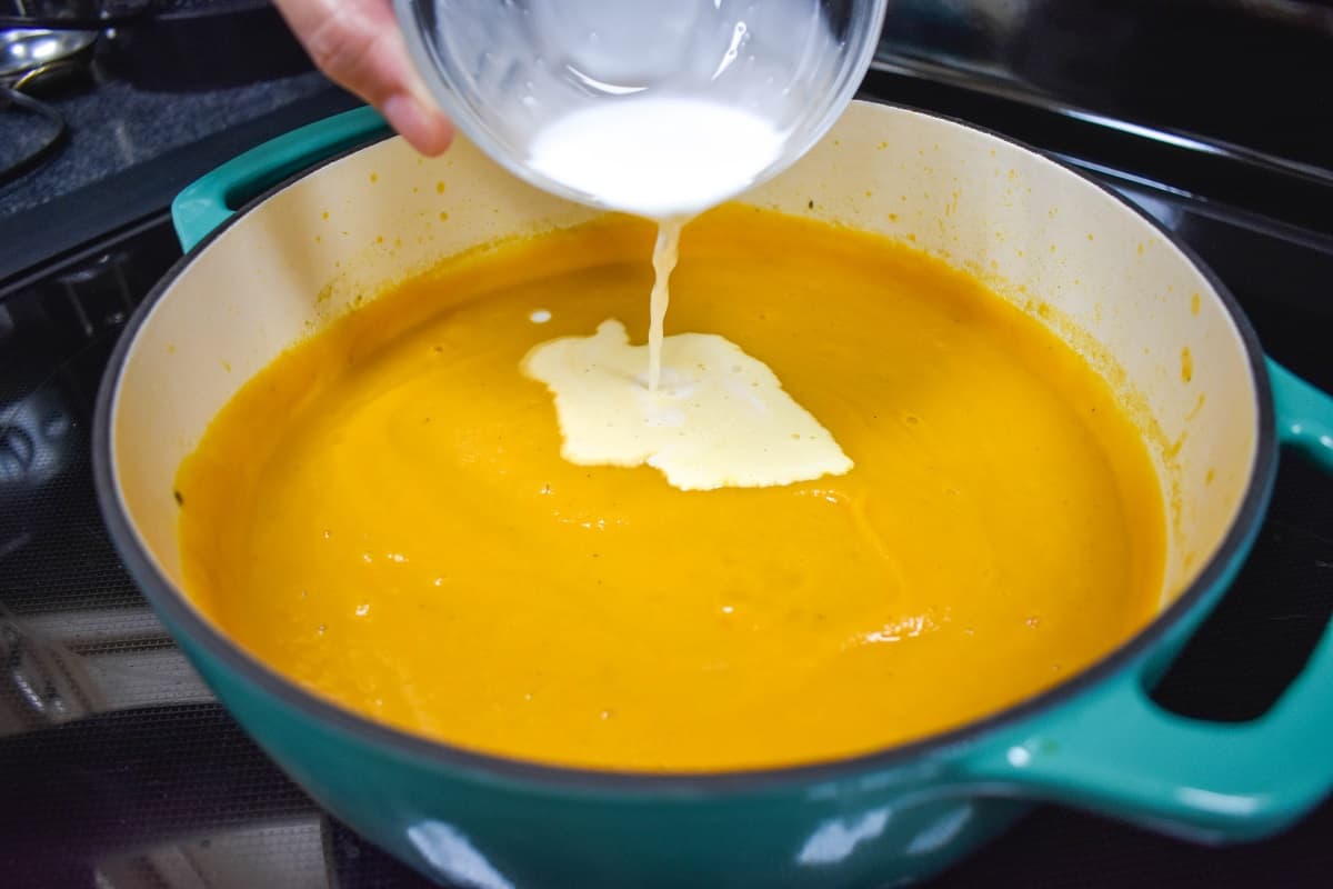 Half and half being added to the sweet potato soup in the pot.