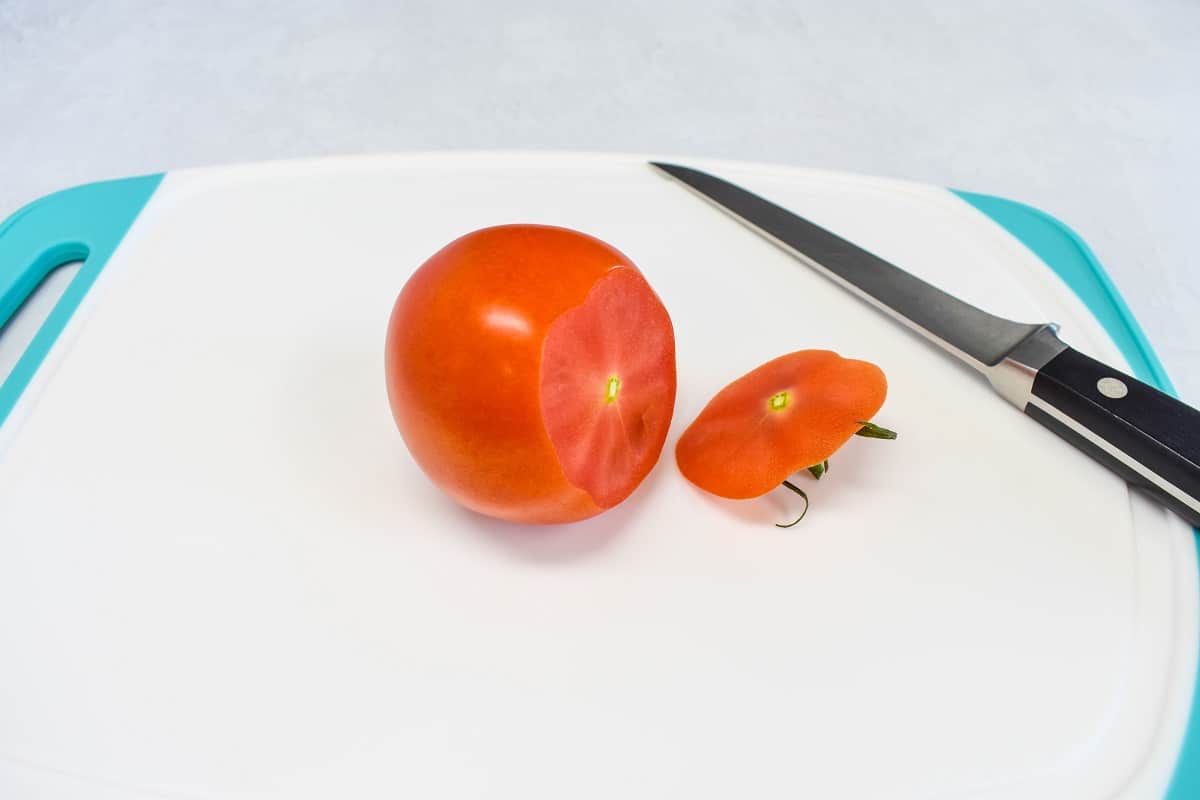 A tomato with one end cut off on a white cutting board.