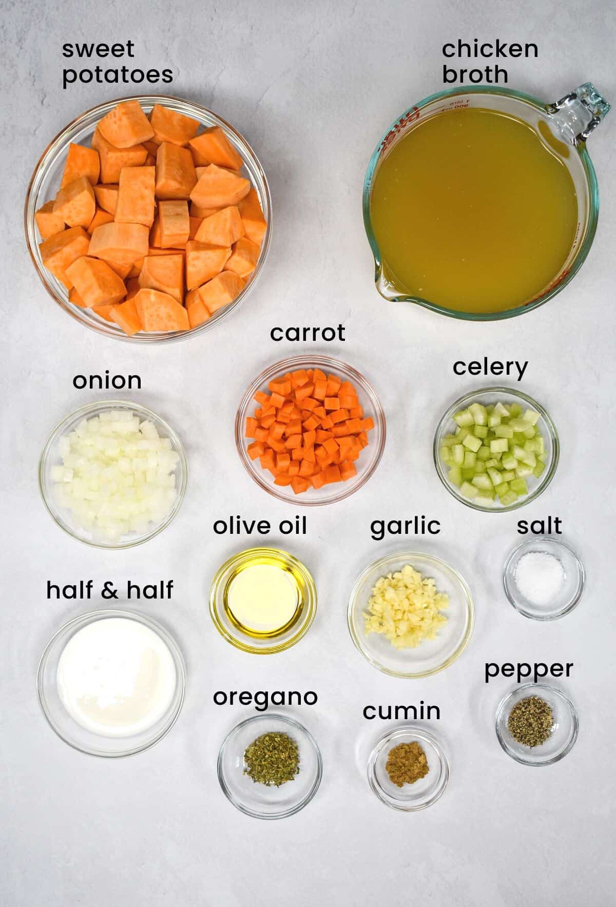 The ingredients for the soup arranged in bowls and set on a white table with each ingredient labeled with black letters.