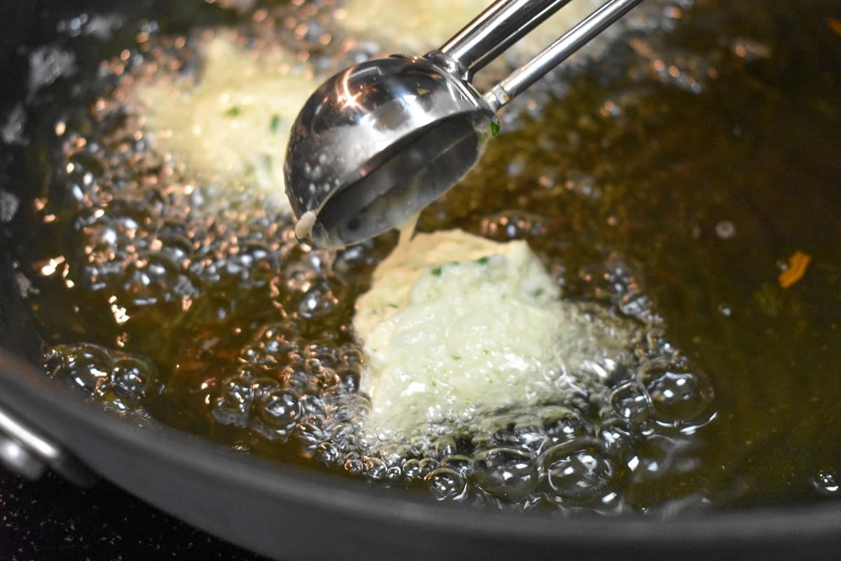 A scoop adding the fritter mixture into hot oil.