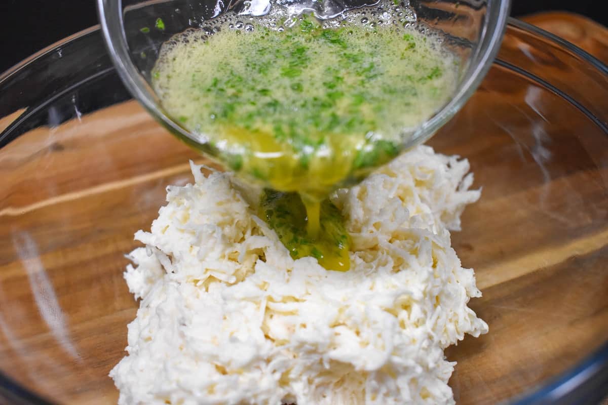 The egg and parsley mixture being added to the shredded malanga in a glass bowl.