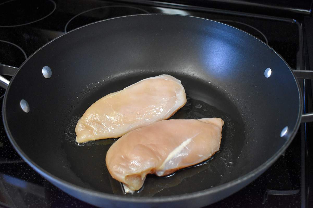 Two pieces of chicken breast on a large, non-stick skillet before browning..