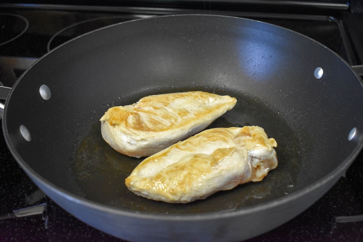 Two pieces of chicken breast on a large, non-stick skillet after browning..