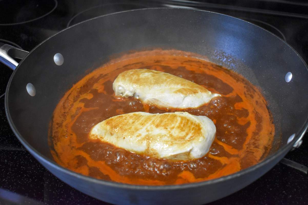 The browned chicken breast in the skillet with tomato sauce.