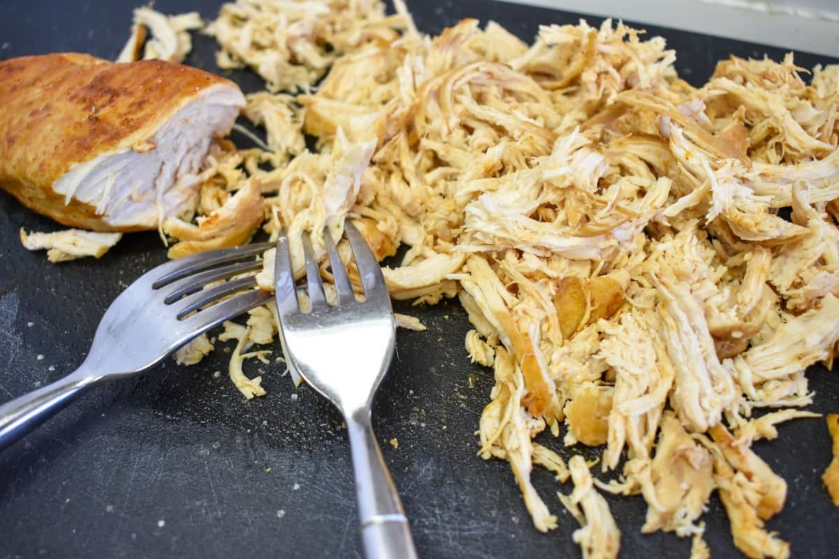 Shredded chicken on a black cutting board with two forks.