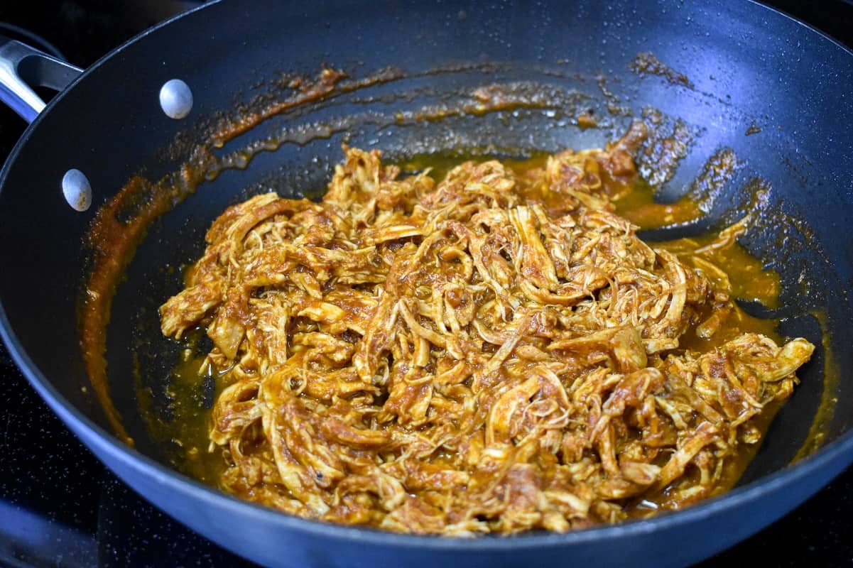 The shredded chicken combined with the tomato sauce in the skillet.