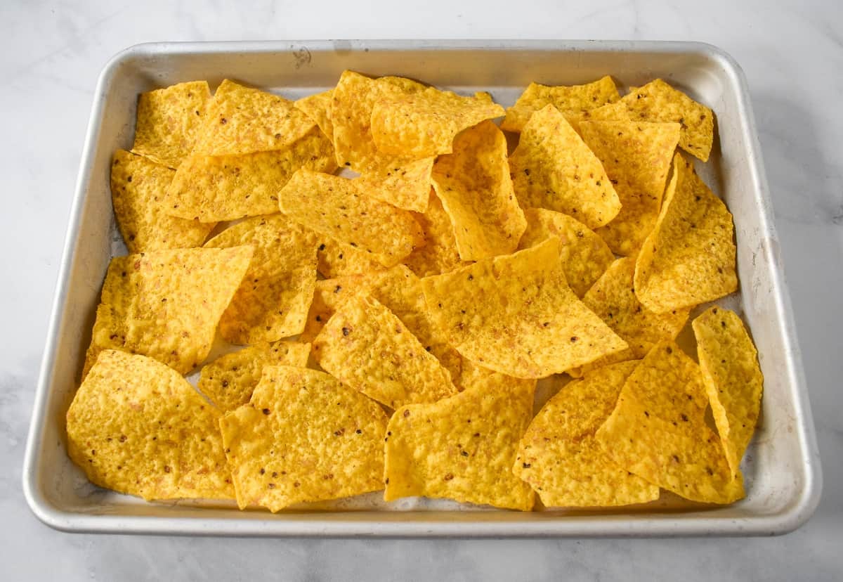 A layer of tortilla chips arranged on a sheet pan.