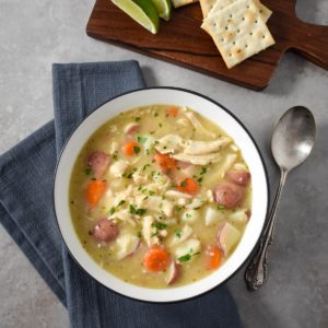 The chicken stew served in a white bowl set on a gray linen with lime wedges and crackers.