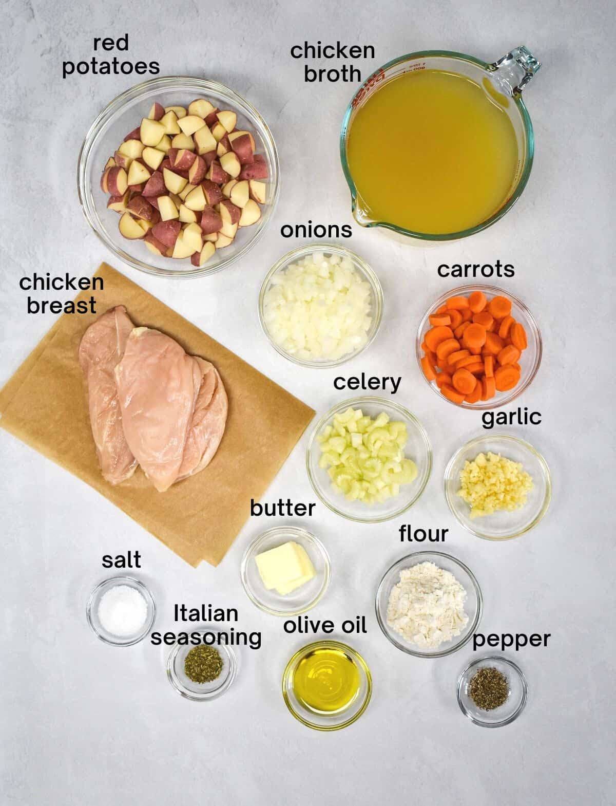 The ingredients for the chicken stew prepped and arranged in bowls on a white table.