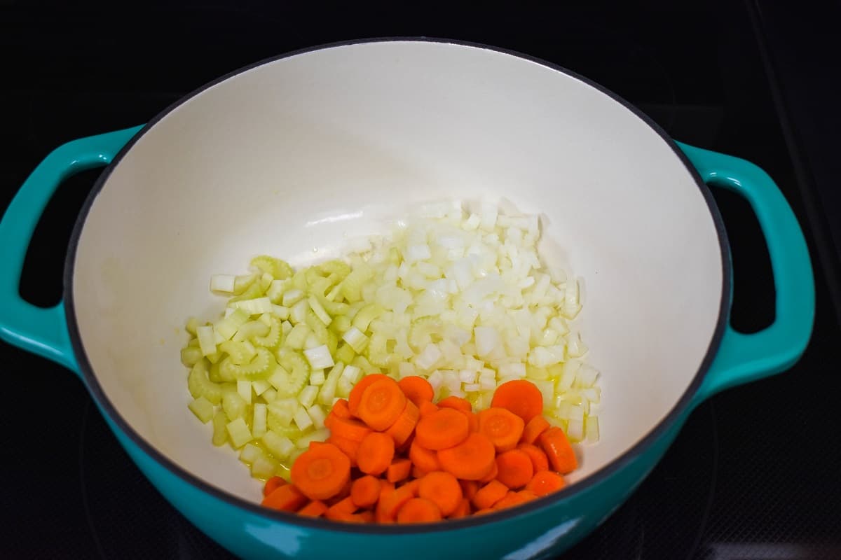 Onions, carrots, and celery cooking in a white and aqua pot.