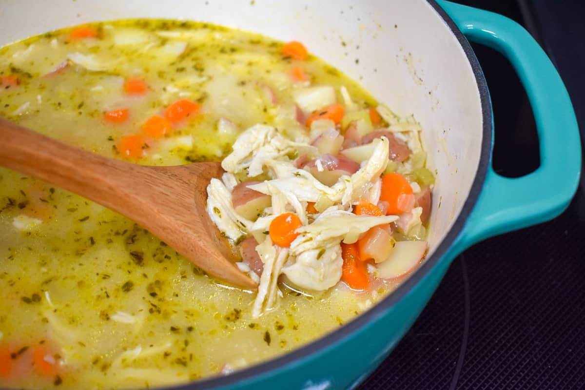 A wooden spoon in the pot showing shredded chicken along with the other ingredients of the stew.