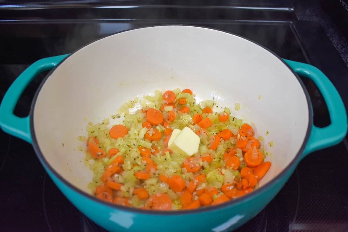 Two pats of butter added to the vegetables in a white and aqua pot.