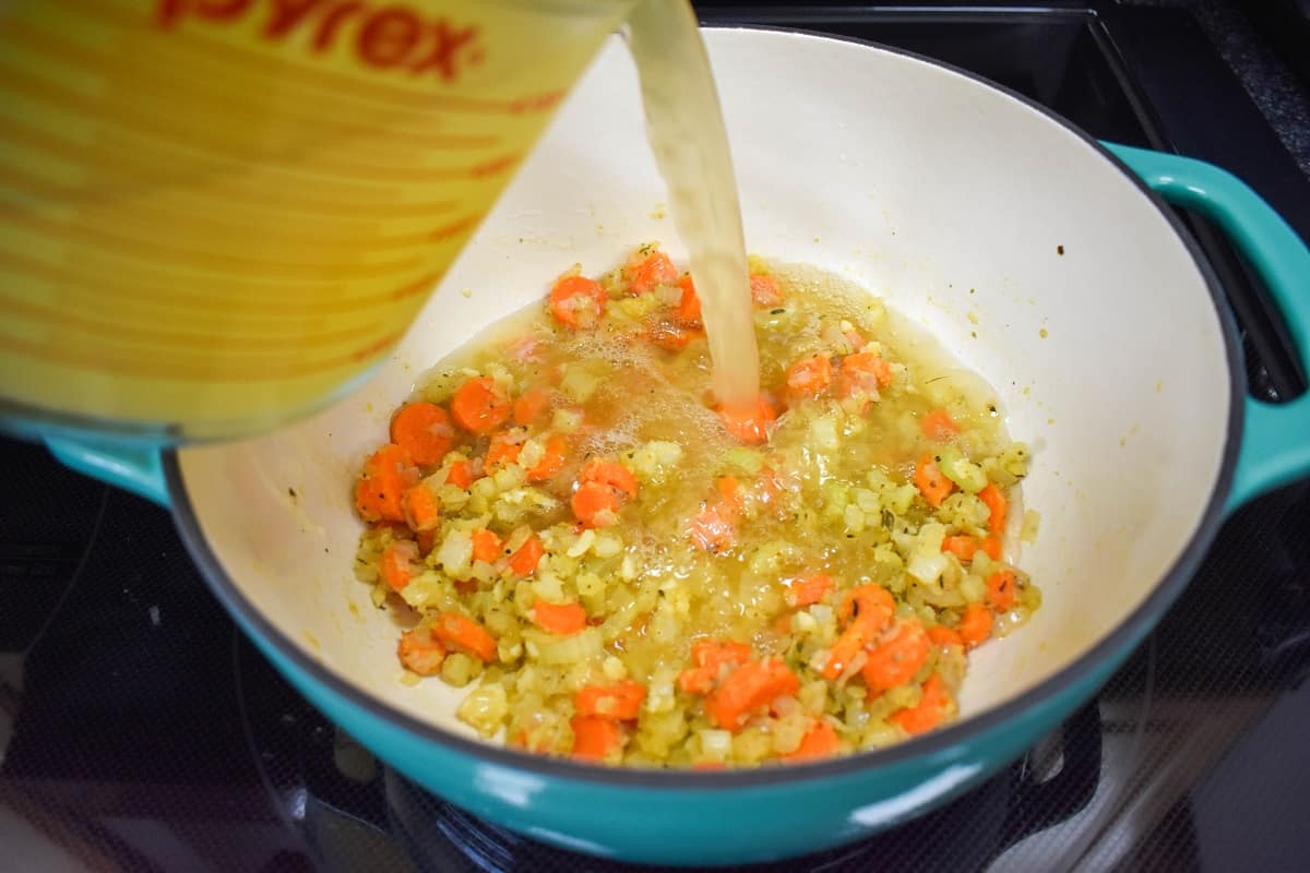 Chicken broth being added to the ingredients in the pot.