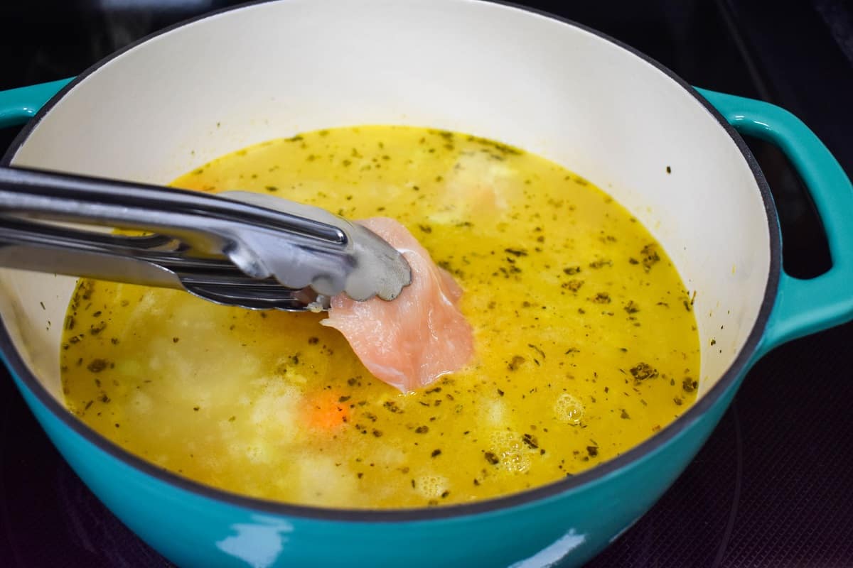 A piece of raw chicken being added to the broth with tongs..