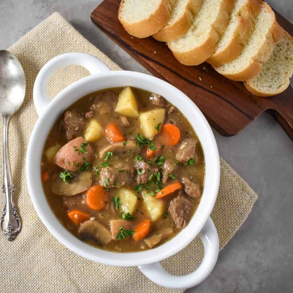 The beef stew served in a white bowl with sliced bread on a small board.