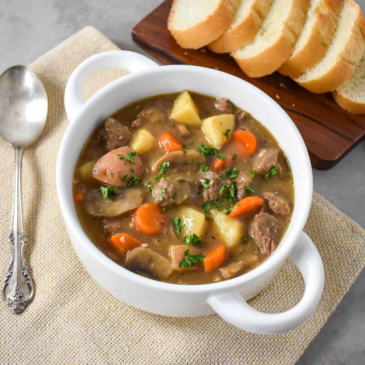 The finished stew served in a white bowl with sliced bread on the side.