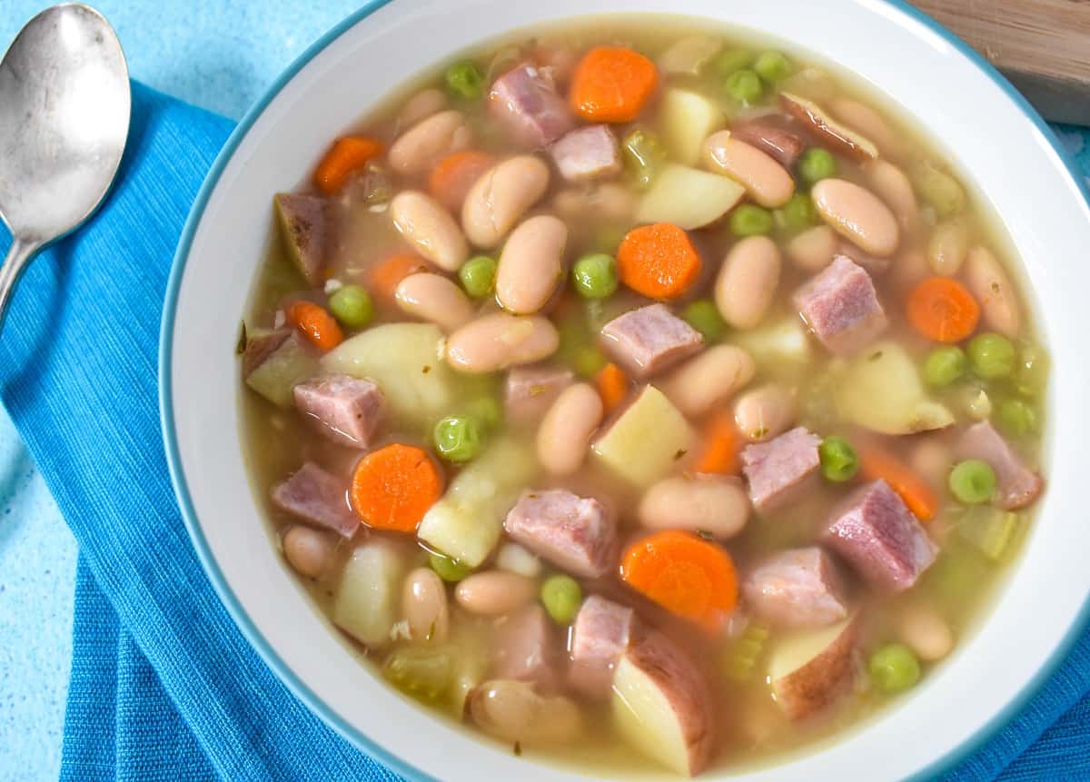 A close up of the ham and bean soup served in a white bowl with an aqua linen.