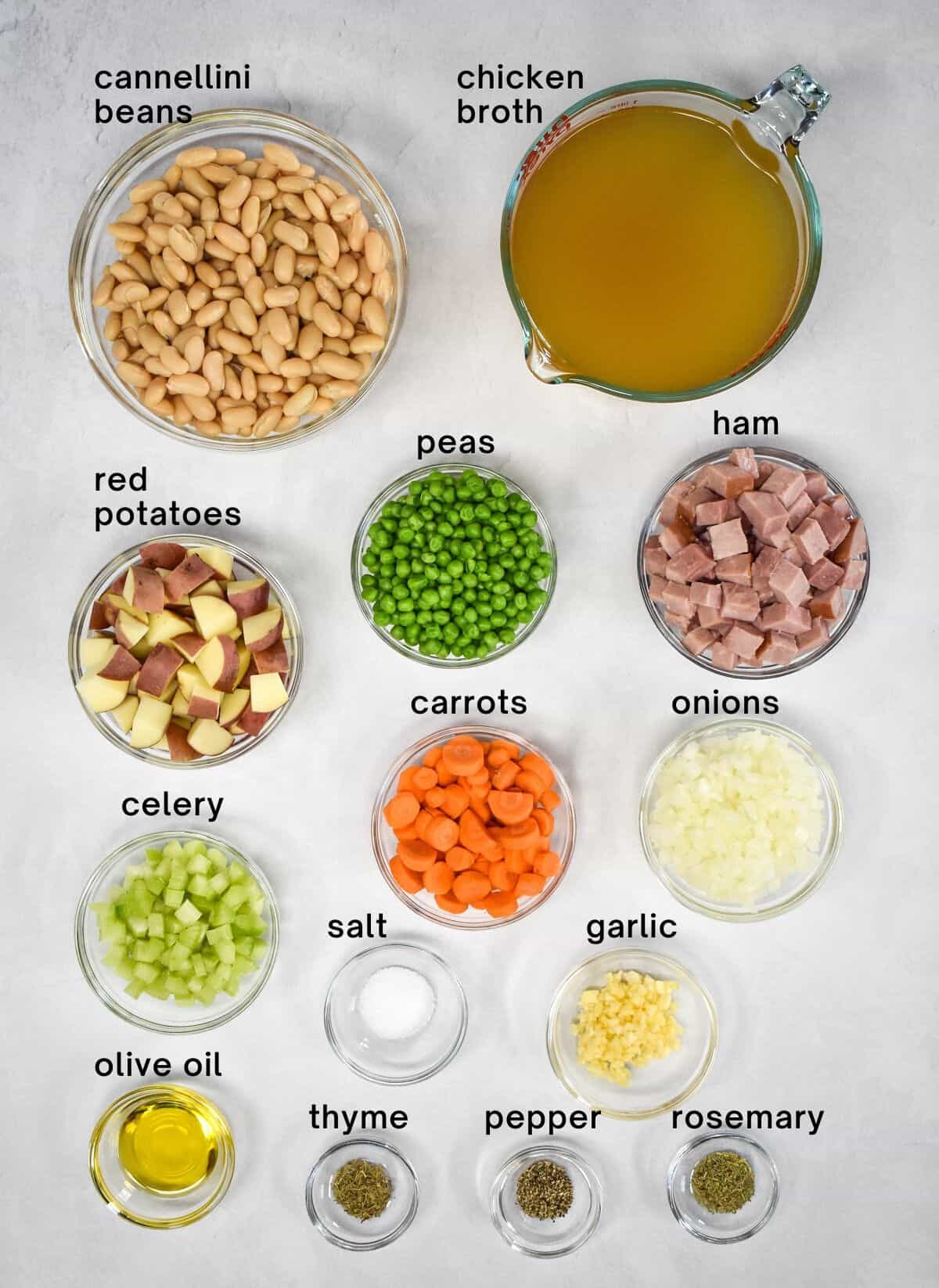 The ingredients for the soup arranged in glass bowls on a white table with each ingredient labeled with small black letters.
