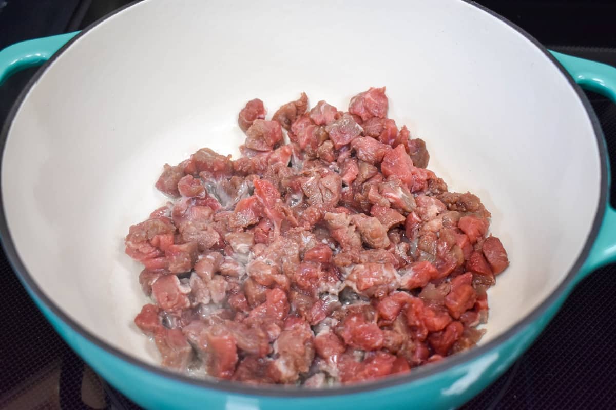 Diced beef cooking in a large enameled, Dutch oven.