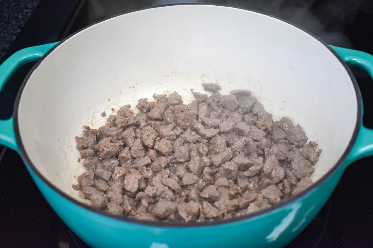 Browned diced beef cooking in a large, enameled Dutch oven.