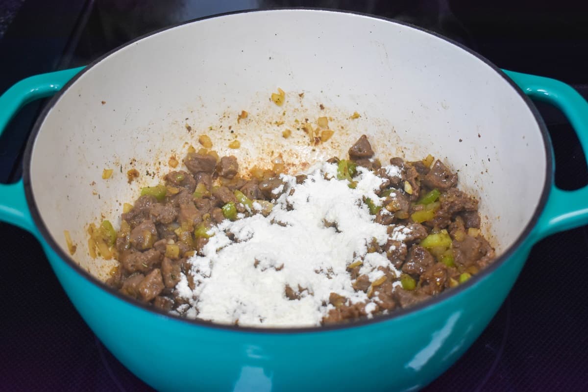 The beef mixture in the pot with flour sprinkled on top of it.