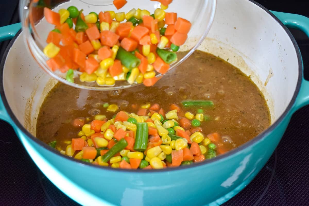 The mixed vegetables being added to the beef mixture in the pot.