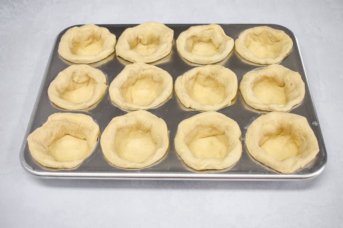 Uncooked biscuits molded in a twelve count muffin tin.