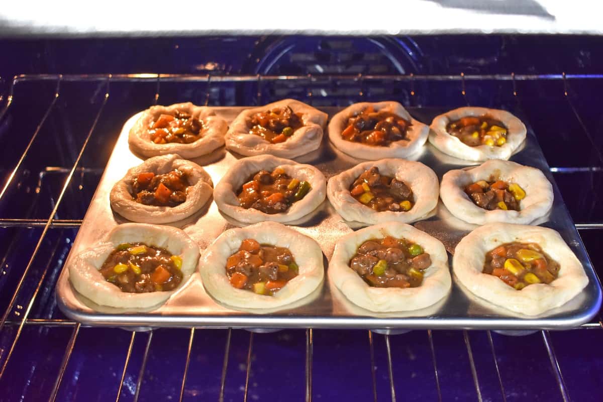 The filled biscuits in the muffin tin placed in the oven.