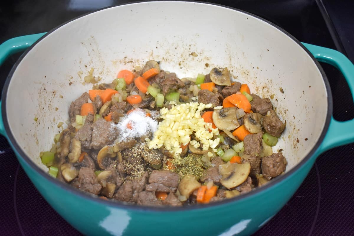 Minced garlic and spices added to the beef and vegetables in the pot.
