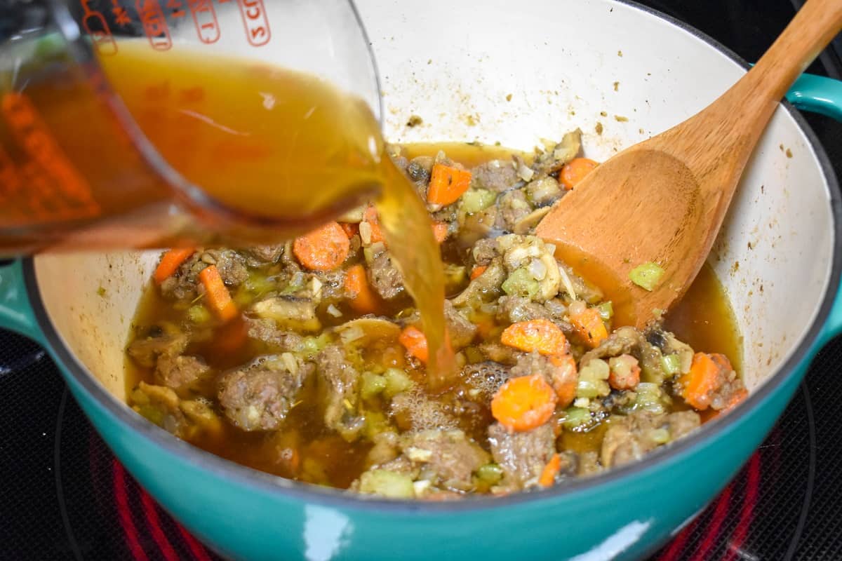 The beef broth being added to the ingredients in the pot.