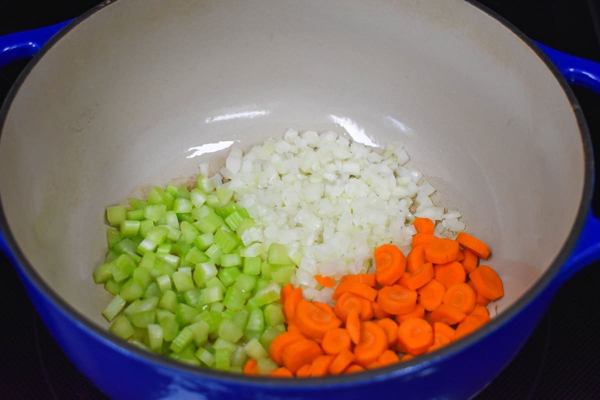 Diced onions, carrots, and celery cooking in a large blue and white pot.