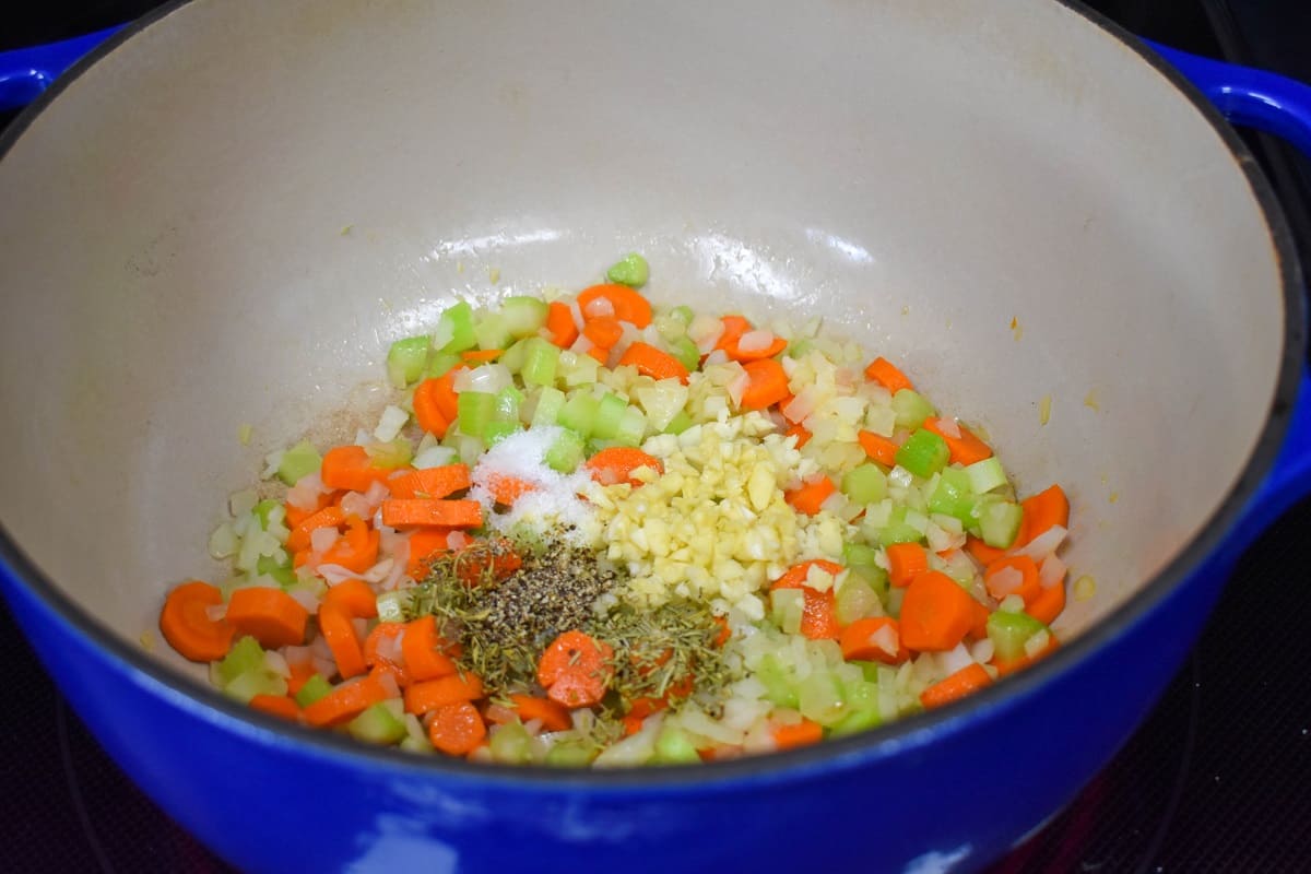 Garlic and spices added to the vegetables cooking in a large blue and white pot.