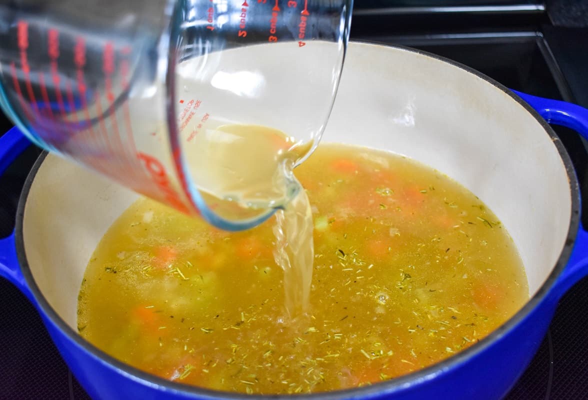 Chicken broth being added to the ingredients in the pot.