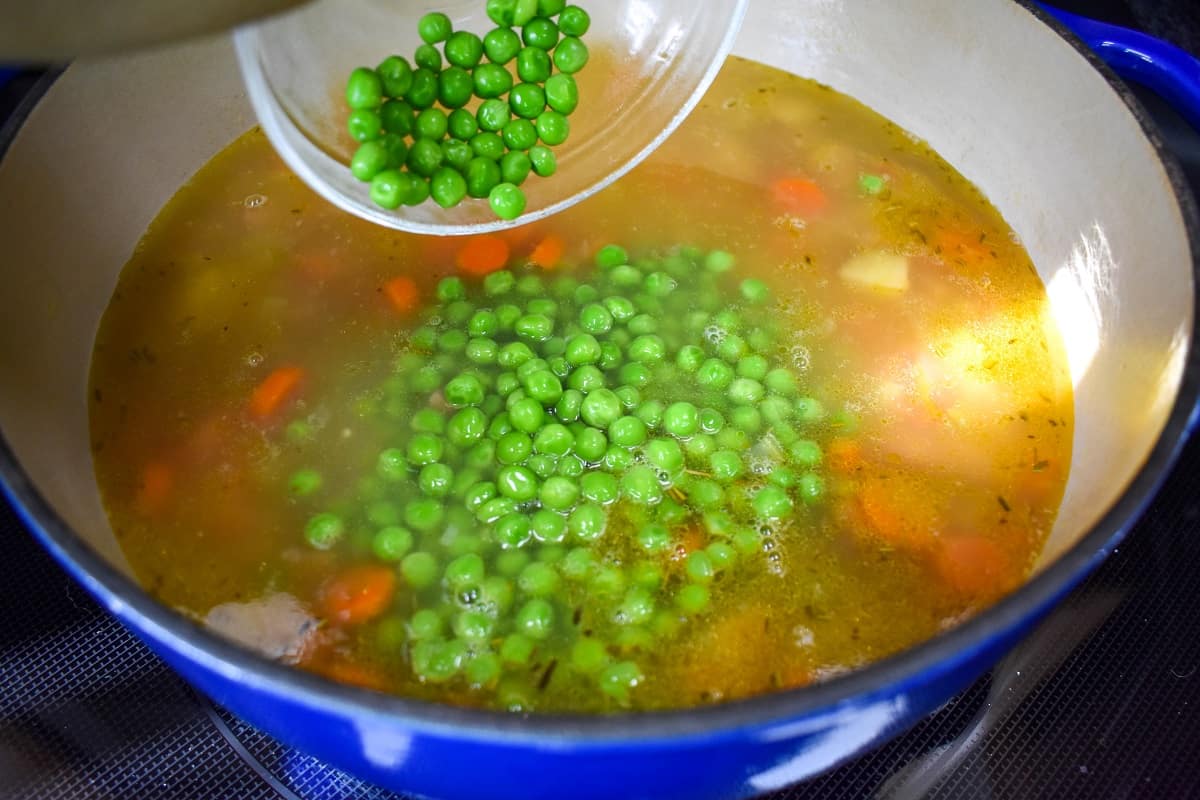 Green peas being added to the soup in the pot.