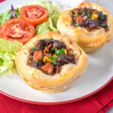 Two mini beef pot pies with a side salad on a white plate set on a red napkin.